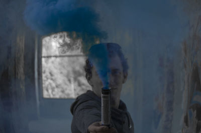 Portrait of man holding blue distress flare in corridor