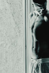 Portrait of shirtless man looking through window