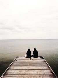 Man sitting on pier at sea