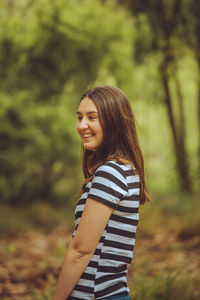 Side view of smiling young woman standing in forest