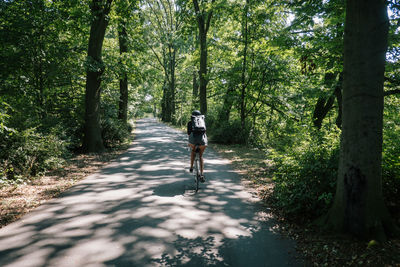 Rear view of woman cycling on road amidst trees in forest