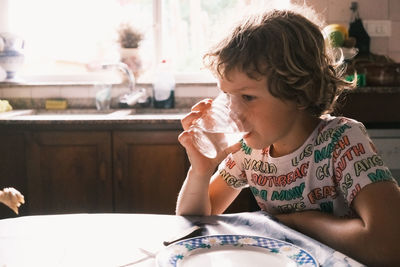 Thirsty boy drinks water from a glass cup, backlit with added film grain.