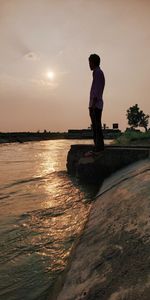 Rear view of man standing by sea against sky during sunset