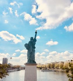 Rear view of statue of liberty over seine river against cloudy sky in paris 