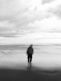 Rear view of man walking on beach against sky