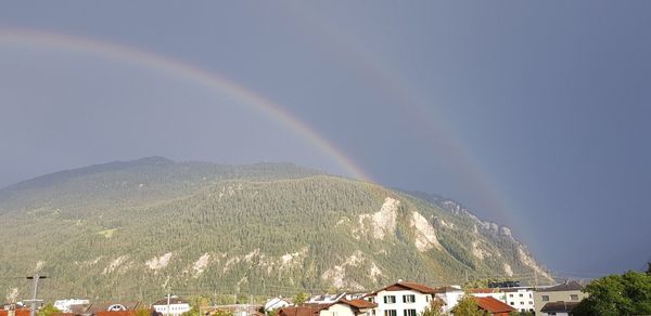 Rainbow over buildings and mountains against sky