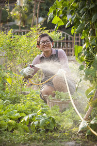 Woman watering plants while sitting at farm