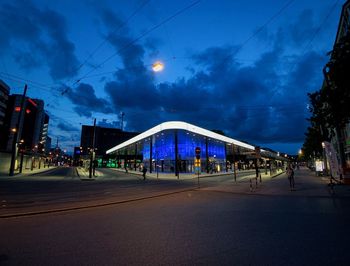 Road by illuminated city against sky at night