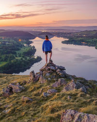 Rear view of man standing on rock against sky during sunset