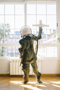 Back view of kid with a real astronaut uniform. he is playing alone with a space shuttle at home