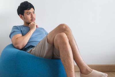 View of man's legs on white bed with tv and plant.