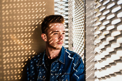 Young man looking through window while sitting against wall