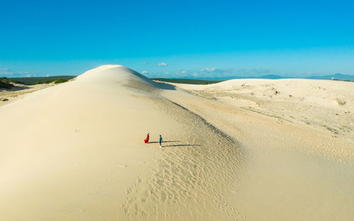 Aerial view of couple standing on sand dunes in desert against clear blue sky