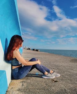 Woman sitting on beach looking at sea against sky