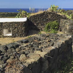 Stone wall by rocks against sky