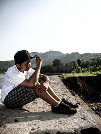 Young man sitting on mountain against sky