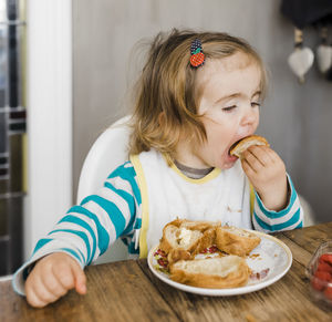 Cute girl eating bread while sitting by table at home