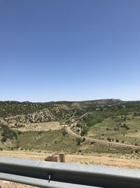 Scenic view of road amidst field against clear blue sky