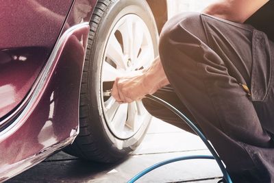 Midsection of mechanic filling air in car tire at garage