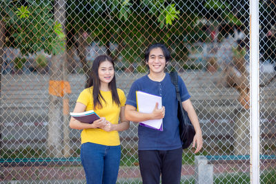 Portrait of a smiling young woman holding chainlink fence