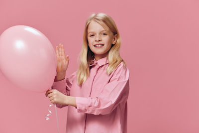 Portrait of young woman holding balloons against pink background