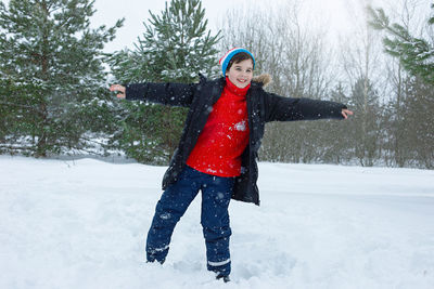 A cheerful teenage boy in a winter park stands in the snow