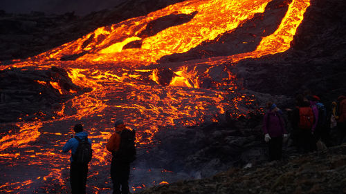 People standing by bonfire on mountain at night