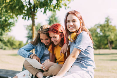 Attractive teenage girls are sitting on a park bench, discussing and smiling. 