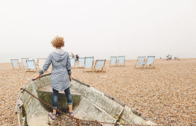 Rear view of woman standing on boat wreck at beach against clear sky