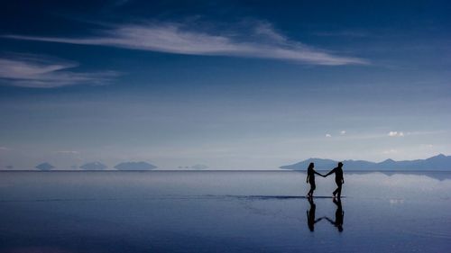 People standing in sea against sky during sunset