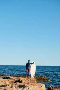 Rear view of friends standing on beach against clear sky