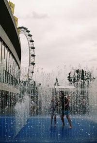 People enjoying at water fountain against sky