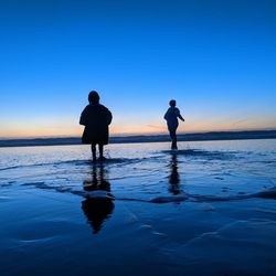 Silhouette men on beach against sky during sunset