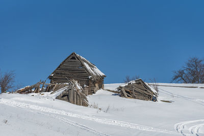 Snow covered field by building against clear blue sky