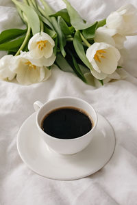 Cup of coffee and white tulips on the white bed sheet close-up