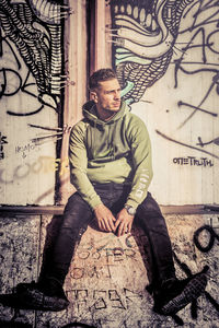 Portrait of young man sitting on wall