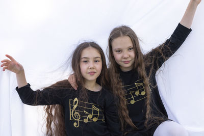 Two smiling girls, sisters with long hair having fun under sheet on grass in park, making tent