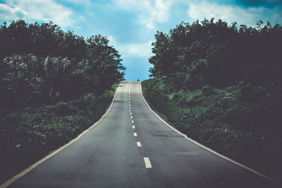 Empty road amidst trees against sky