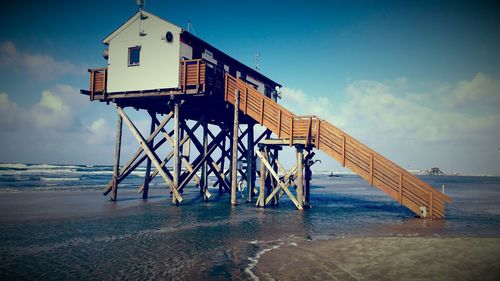 Stilt house at beach against sky