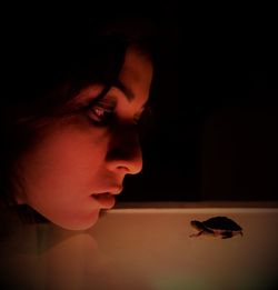 Close-up of woman looking at turtle on table against black background