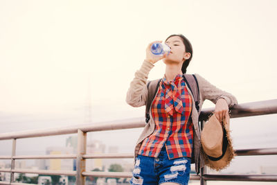 Young woman drinking water while leaning on railing