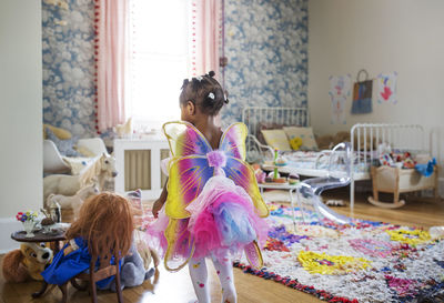 Rear view of girl dressed in fairy costume walking in bedroom