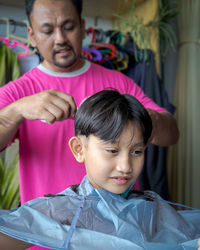 Asian child getting haircut at home from the father.