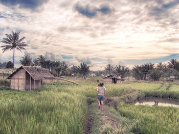 People walking on grassy field against cloudy sky