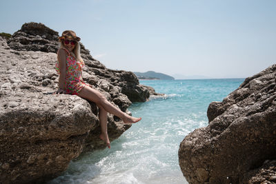 Young woman on rock by sea against sky