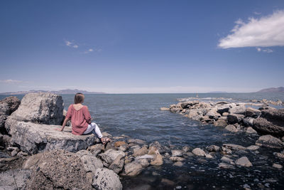 Woman sitting on rock at beach against sky