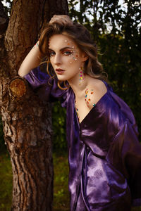 Portrait of beautiful woman standing by tree trunk