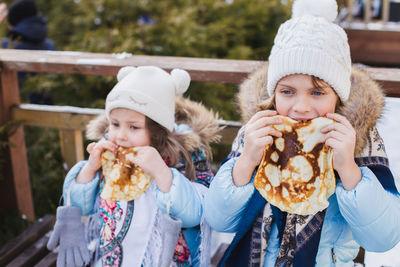 Cute sisters eating food while standing outdoors