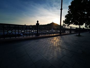 Silhouette people on footpath by street against sky at sunset