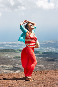Young beautiful woman, dressed in the red dress fluttering in the wind, on the panoramic background